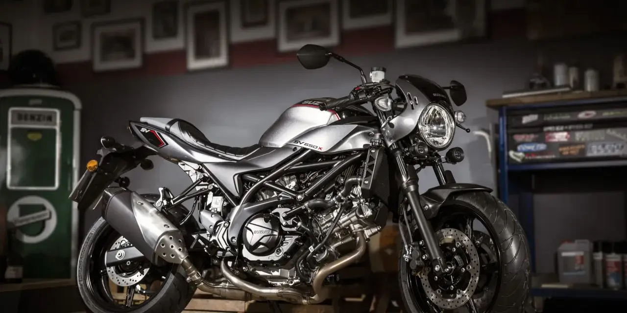 Srebrny motocykl Suzuki SV650X z czarną ramą i detalami, stojący w garażu.
