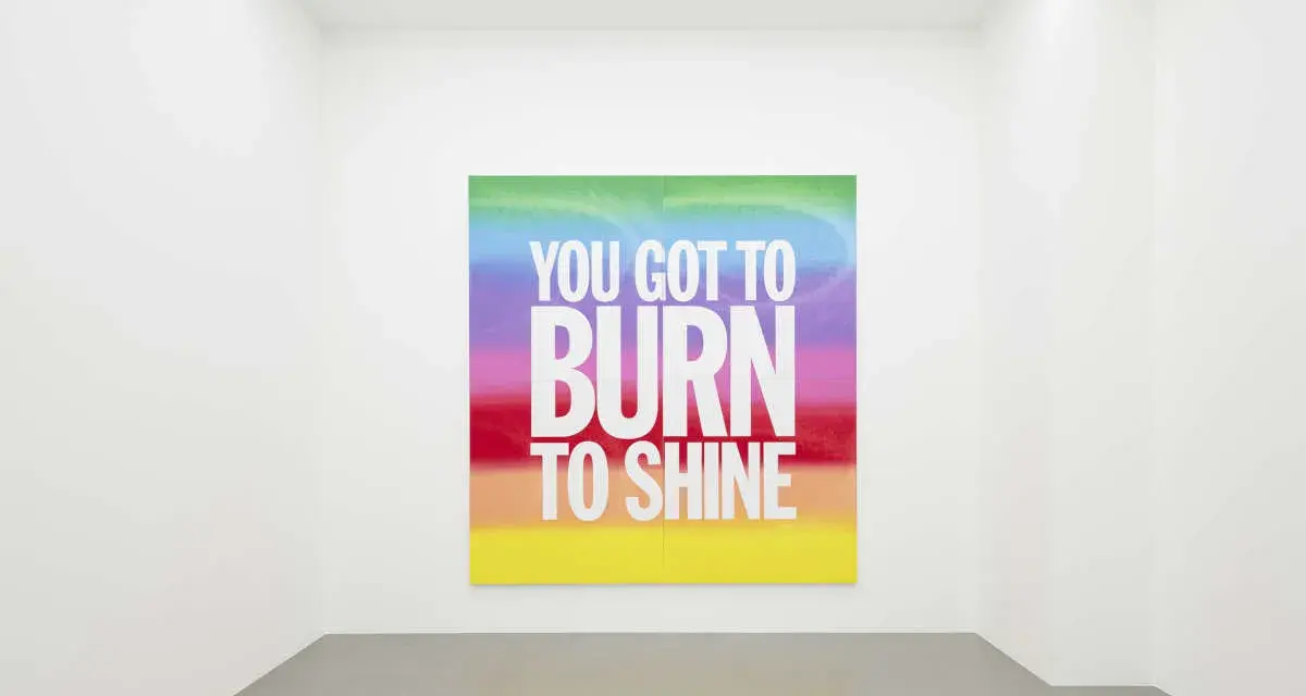 Œuvre de John Giorno dans une galerie, avec le message "YOU GOT TO BURN TO SHINE" sur un fond arc-en-ciel.