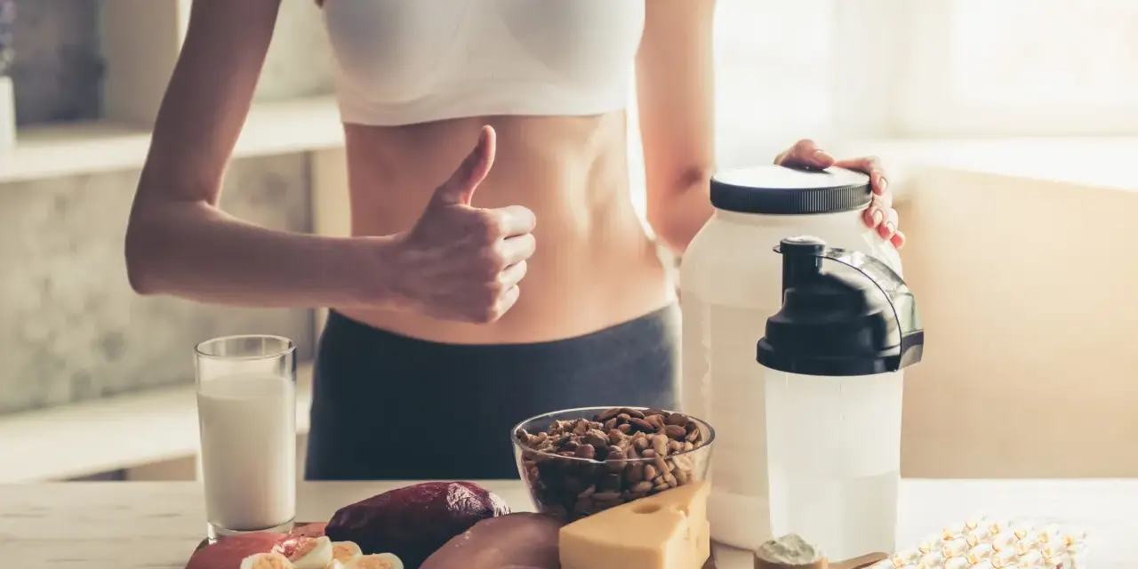 Kobieta z kciukiem w górę prezentuje produkty wspierające dietę wysokobiałkową: mięso, rybę, jajka, ser, orzechy, mleko i suplementy.