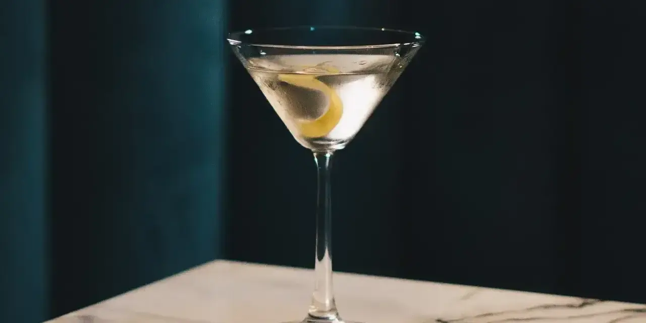Elegancki gin z wermutem, ozdobiony skórką cytryny, czeka na stole z marmurowym blatem.