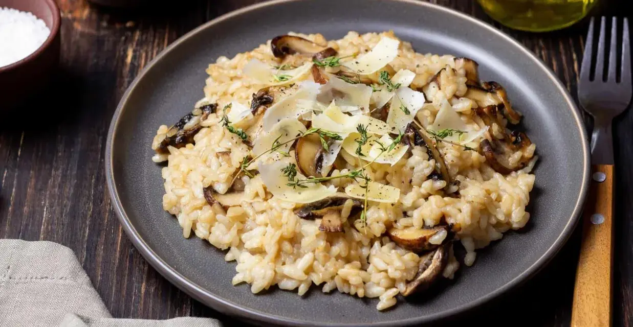 Kremowe risotto z pieczarkami, posypane parmezanem i ziołami, na ciemnym talerzu.