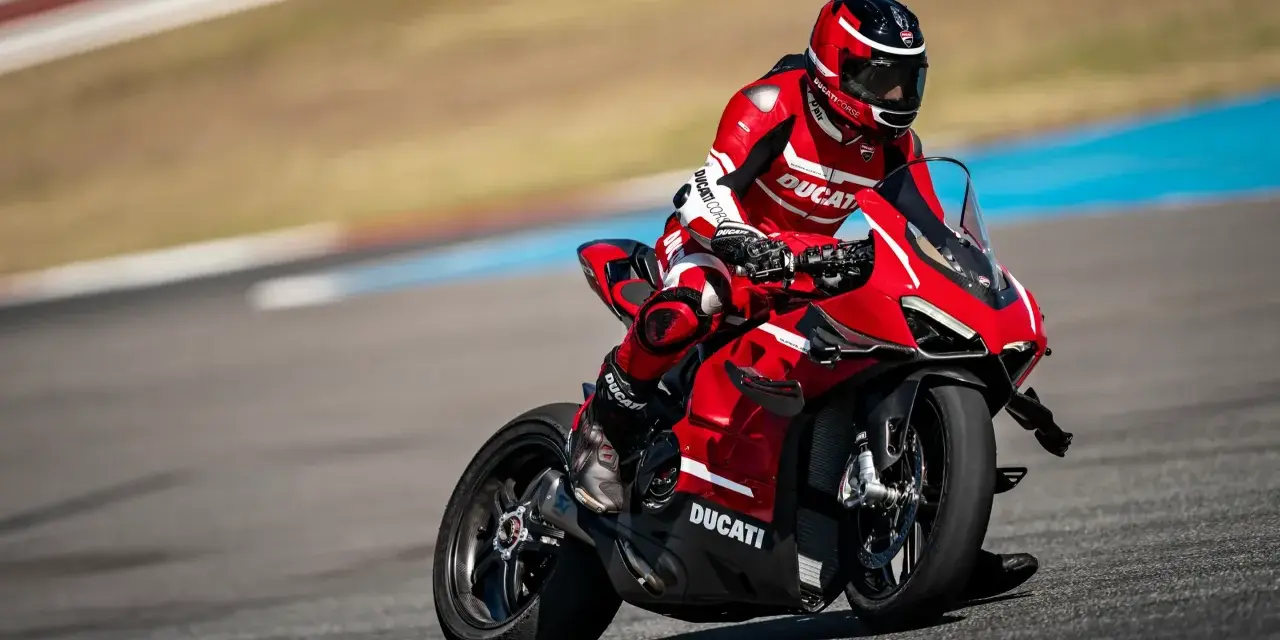 Motocyklista w czerwonym kombinezonie śmiga na torze wyścigowym na swoim czerwonym Ducati Panigale V4.