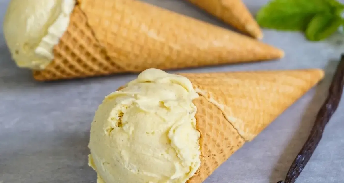 Vanilleeis selbst machen mit Eismaschine: Cremiges Eis in Waffeln, daneben eine Vanilleschote und Minze.