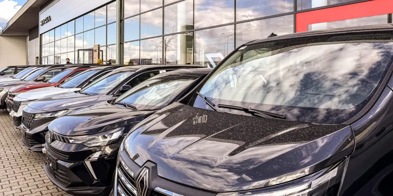 Rząd nowych samochodów na placu. W tle budynek salonu Dacia. Sprawdź autoplac opinie przed zakupem.