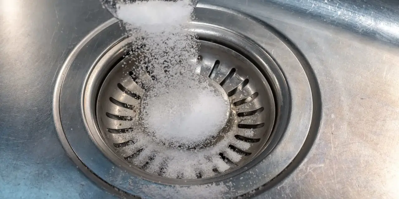 Salt hälls ner i diskhoavloppet. En skopa med salt sprids över silen.