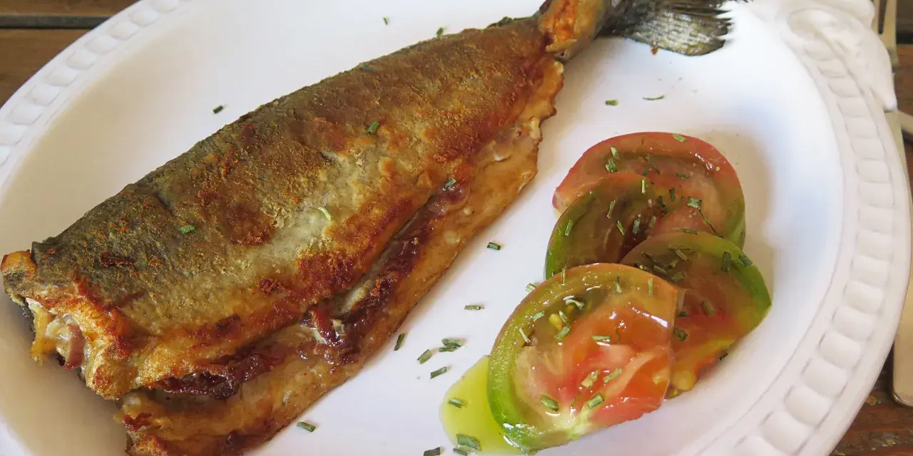 Trucha a la navarra dorada y crujiente, servida con rodajas de tomate fresco y hierbas aromáticas.
