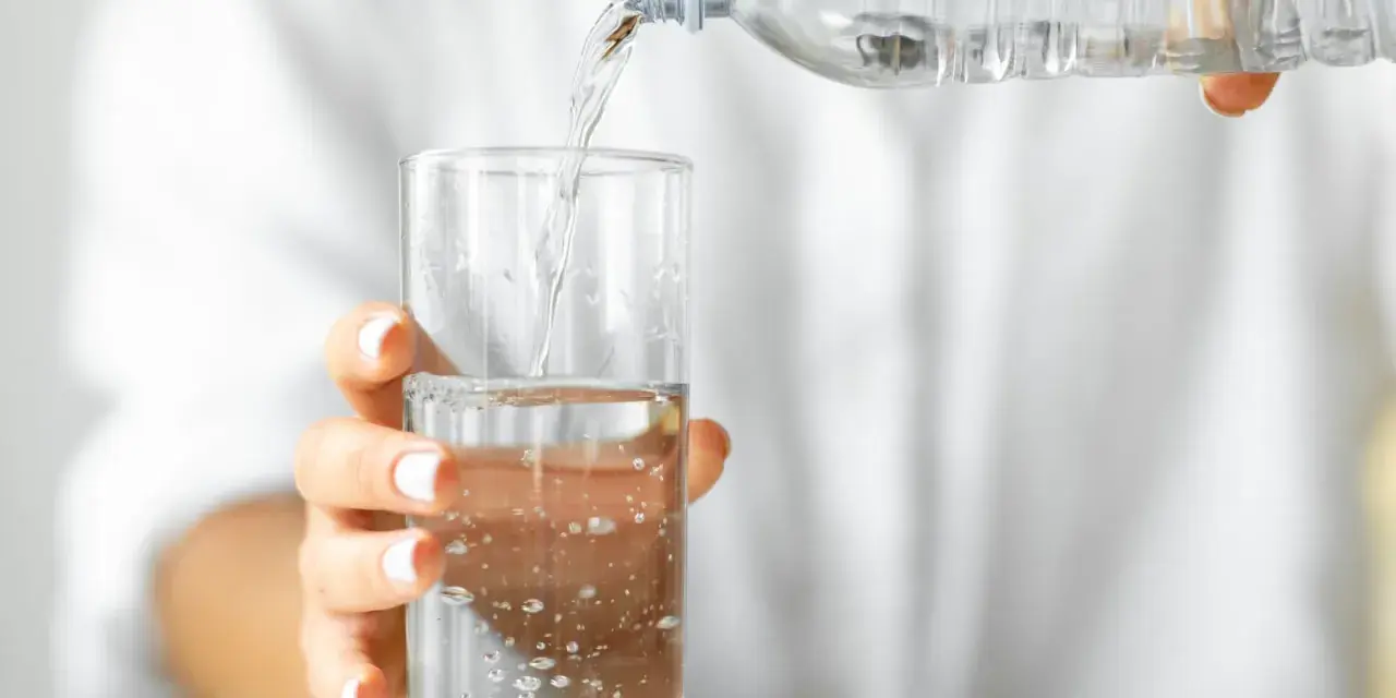 Eine Hand hält ein Glas, in das kohlensäurehaltiges Mineralwasser gegossen wird.