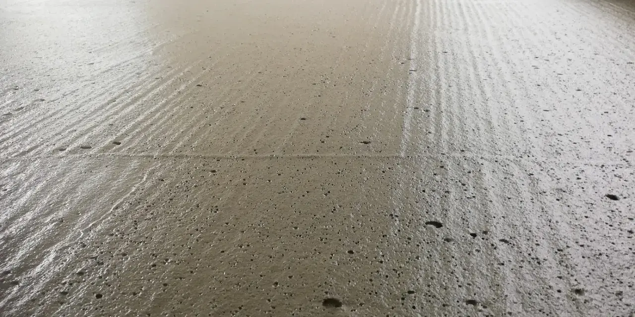 Świeżo wylany, wilgotny **pianobeton** na budowie, z widocznymi śladami po zacieraniu i drobnymi pęcherzykami powietrza.