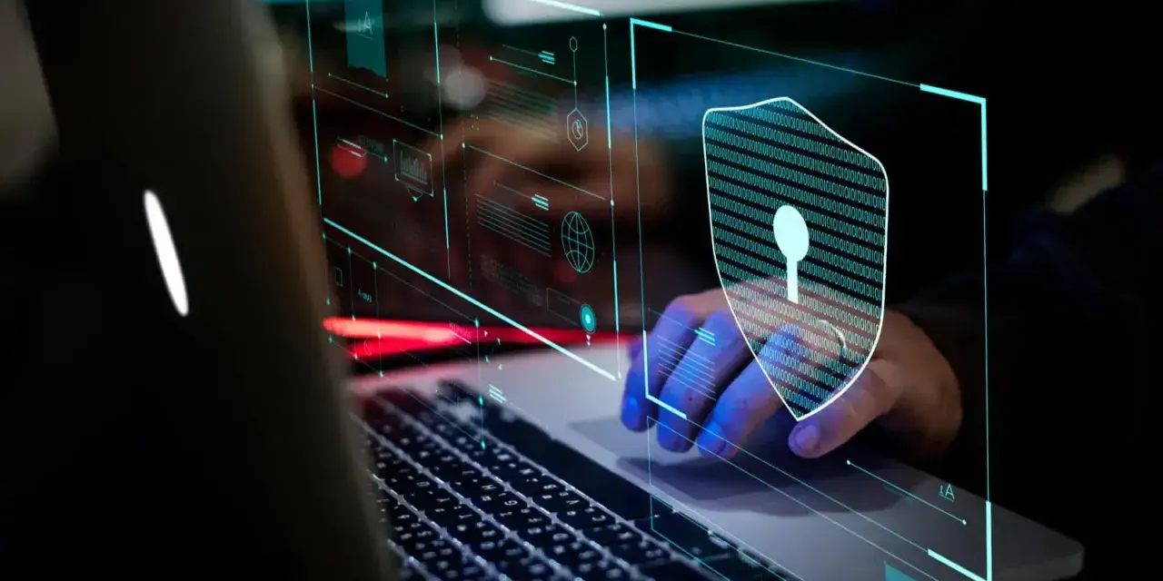 Mano sobre teclado de portátil, con un escudo digital de ceros y unos, simbolizando la seguridad informática.
