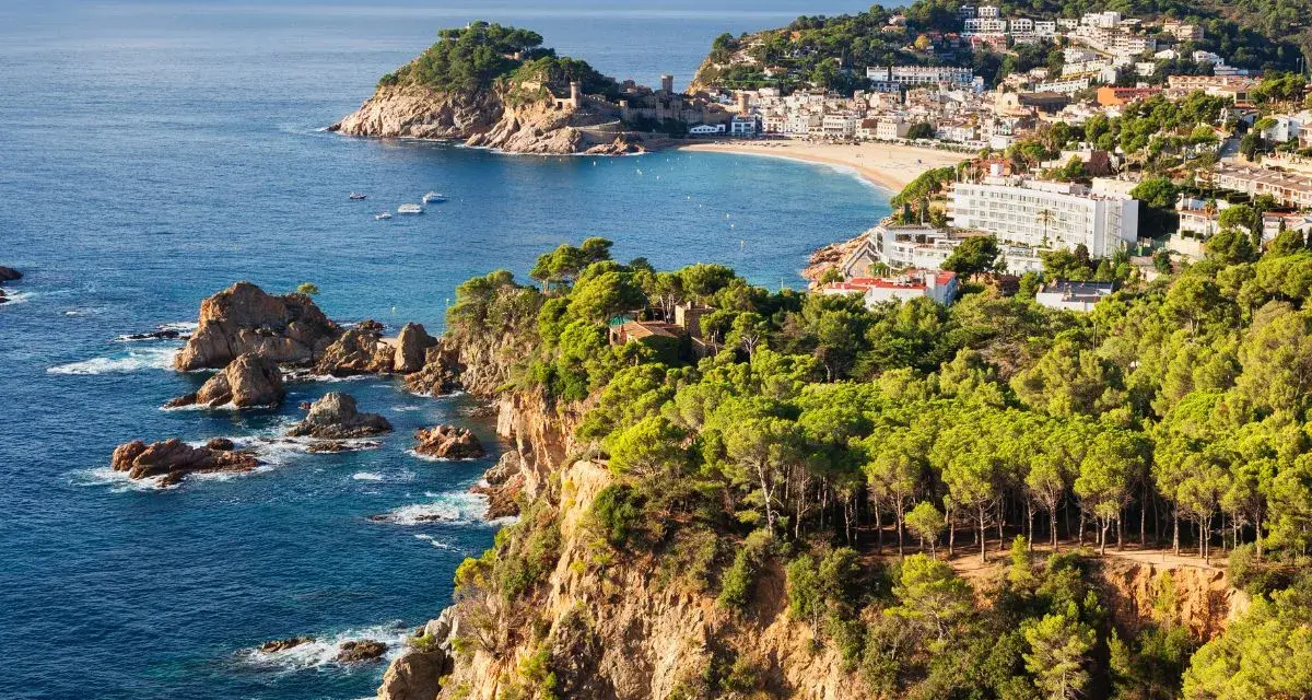 Scenic view of the Costa Brava coastline, a perfect stop on the way to Barcelona, with rugged cliffs, pine forests, and a charming town nestled by the sea.