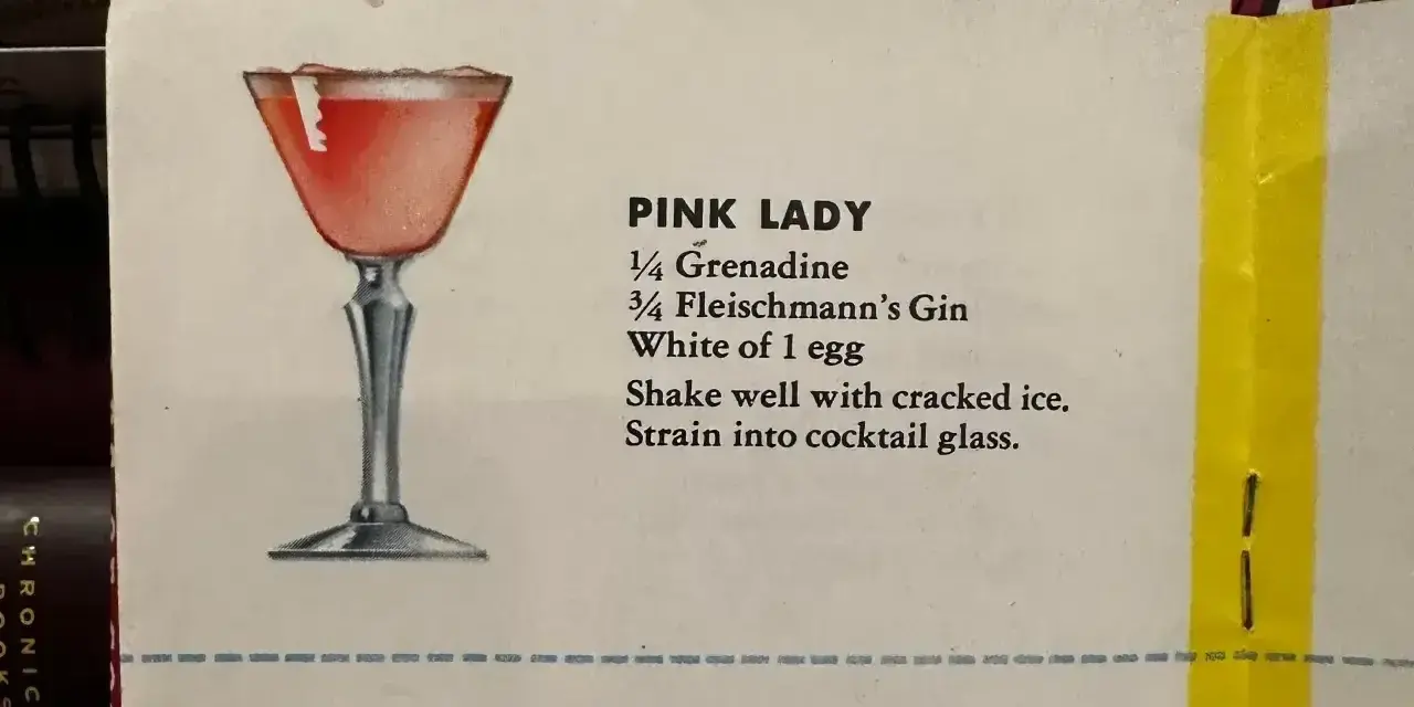 Elegancki kieliszek z różowym drinkiem Pink Lady, obok przepis na jego przygotowanie: grenadyna, gin i białko jaja.