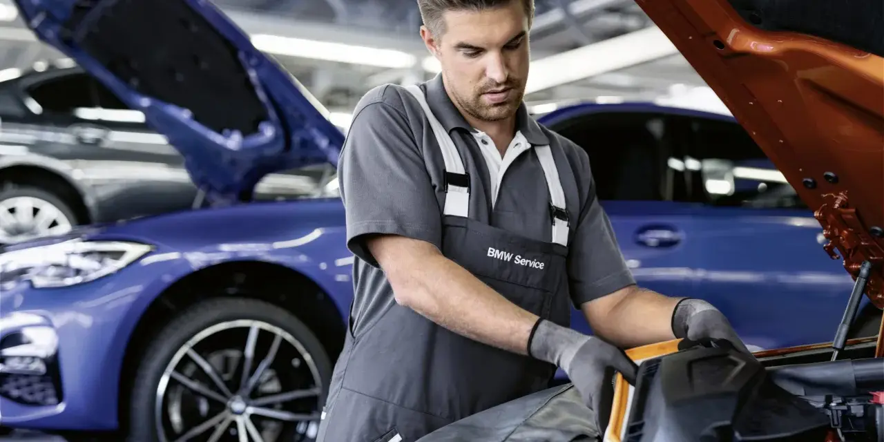 Mechaniker mit BMW Service Kleidung arbeitet an einem blauen BMW. Transparente Kosten für BMW Service.