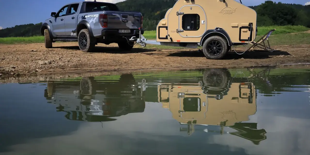 Srebrny Ford Raptor z przyczepą wyprawową Lifestyle Camper nad jeziorem.