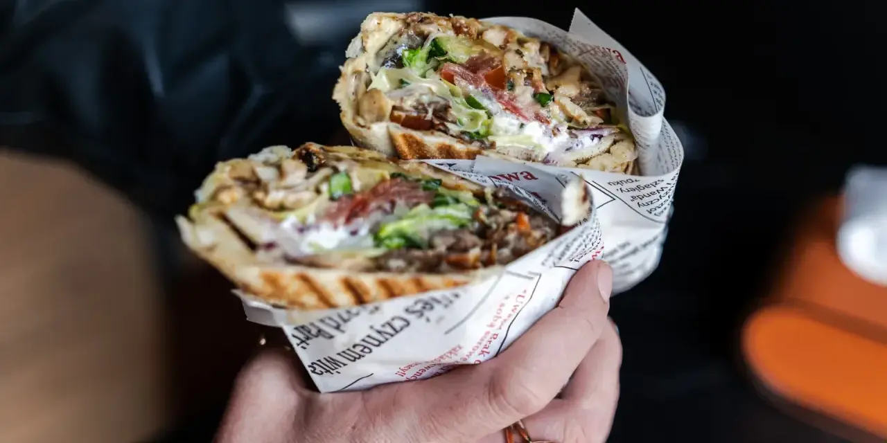 Pyszny kebab z Bukowiny Tatrzańskiej, pełen mięsa, warzyw i sosu, zawinięty w papier z gazetowym nadrukiem.