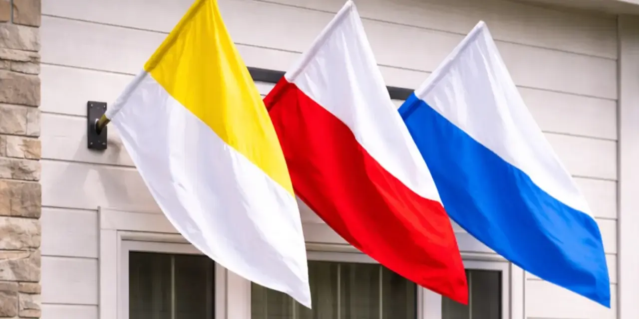 Trzy flagi: żółto-biała, czerwono-biała i niebiesko-biała, powiewają na wietrze. To może być flaga kościelna lub symbol parafii.