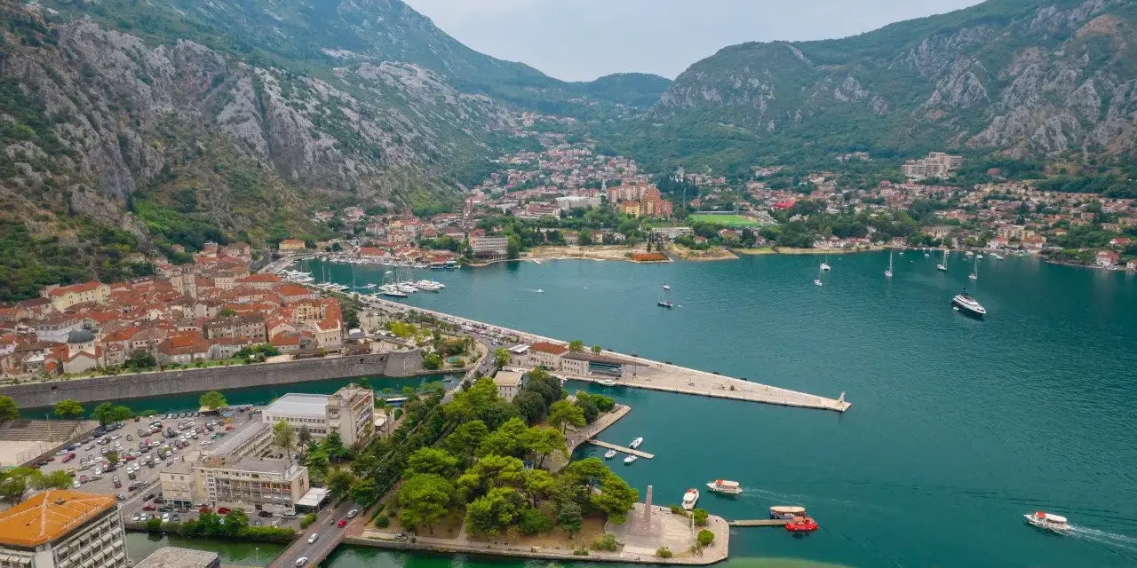Widok na zatokę z górami w tle, miasto Kotor w Czarnogórze, z łodziami i budynkami.