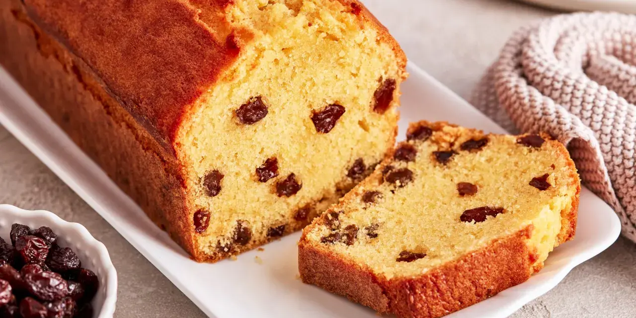 Ein saftiger Rosinenkuchen mit goldbrauner Kruste, auf einem weißen Teller angerichtet. Rosinen sind gut sichtbar im Teig verteilt.