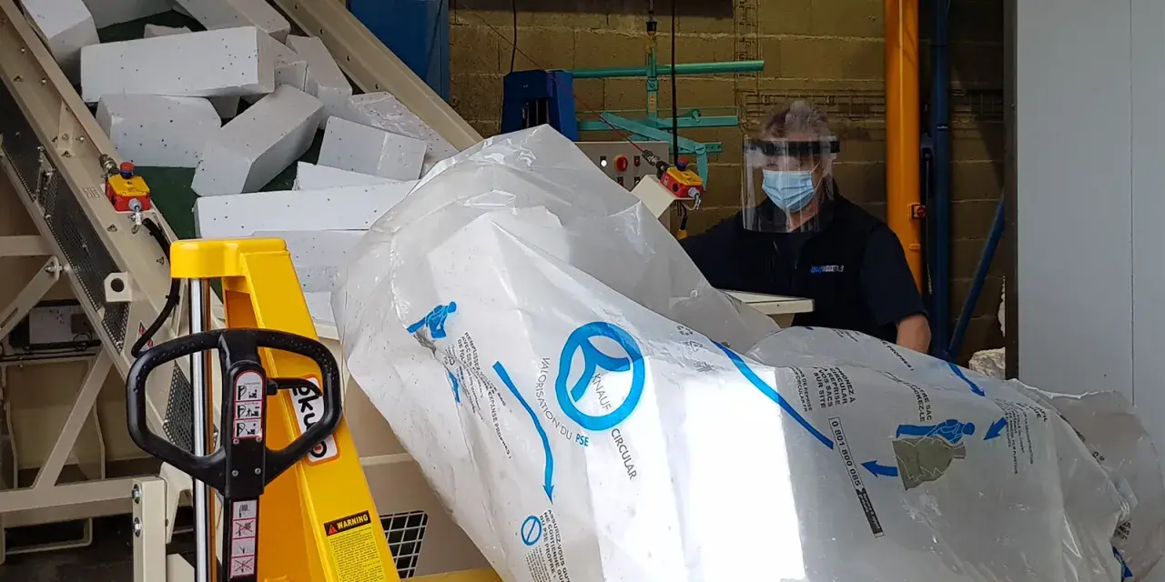 Pracownik w masce i przyłbicy przygotowuje styropian do recyklingu. Duży worek z logo Knauf Circular symbolizuje proces recyklingu styropianu.