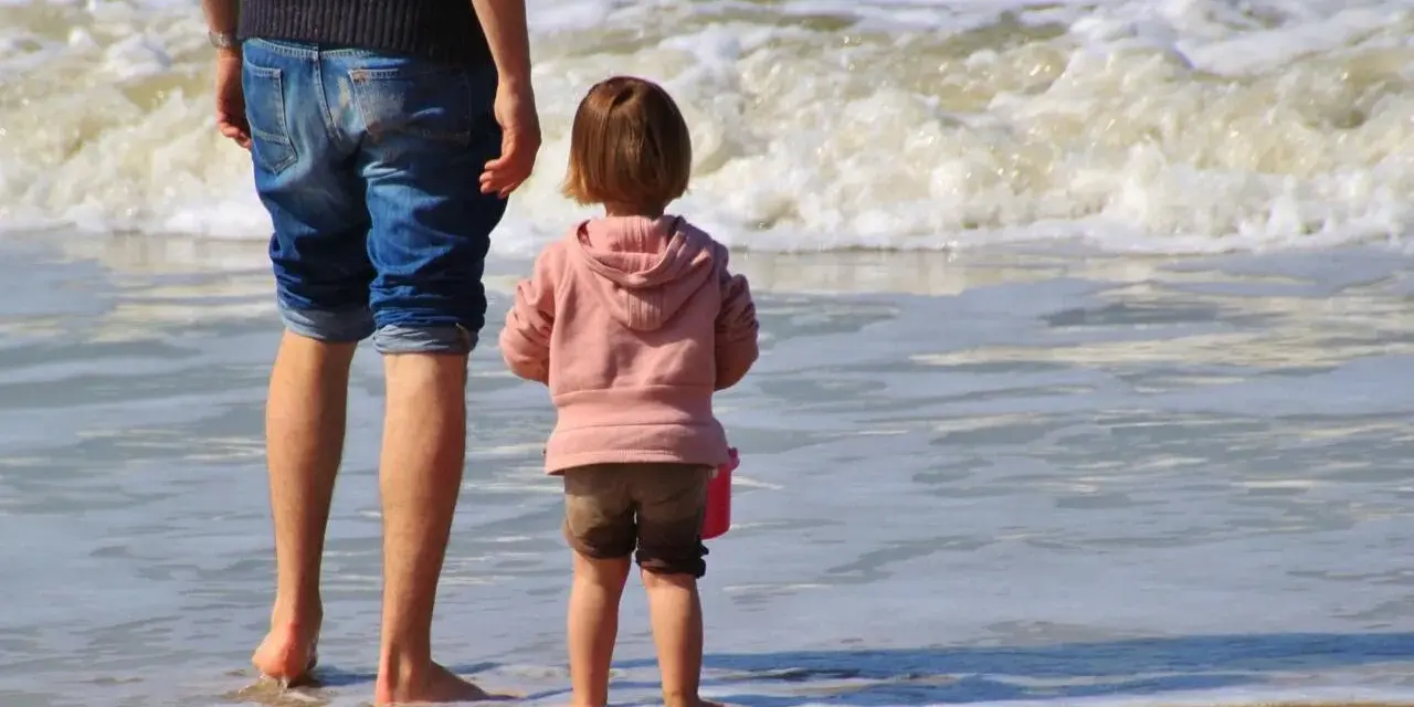 Ojciec i dziecko na plaży, cieszący się wspólnym urlopem ojcowskim 9 tygodni.