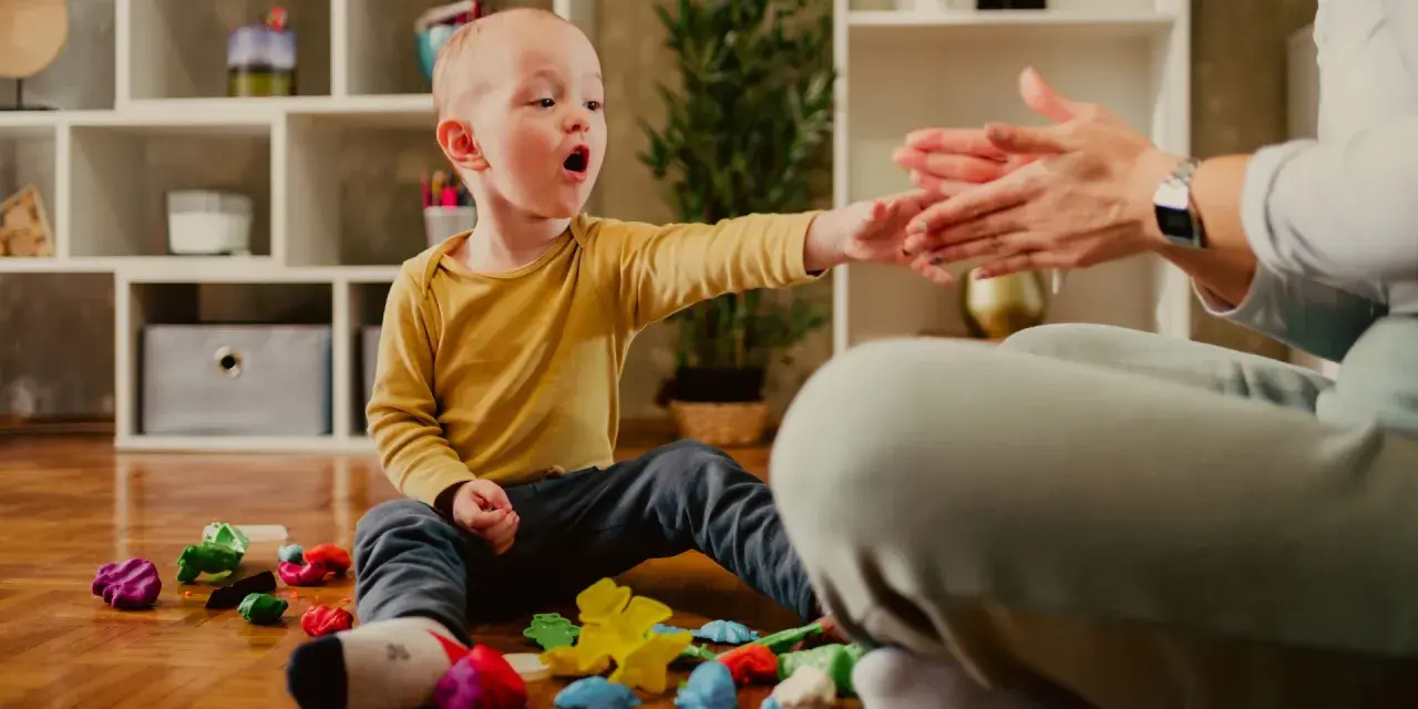 Chłopiec z nadwrażliwością sensoryczną bawi się plasteliną, jego dłoń wyciągnięta w stronę dłoni dorosłego.