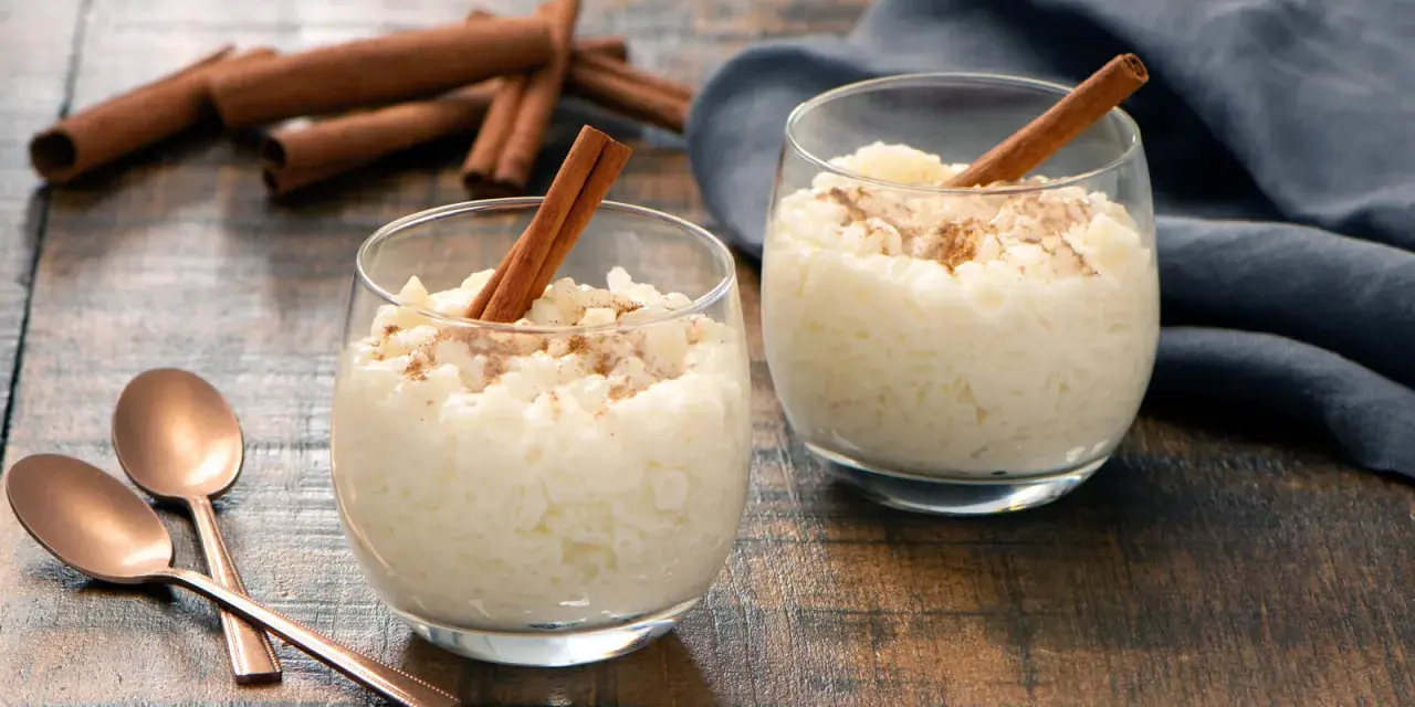 Dos copas de cremoso arroz con leche, espolvoreado con canela y decorado con una rama de canela.