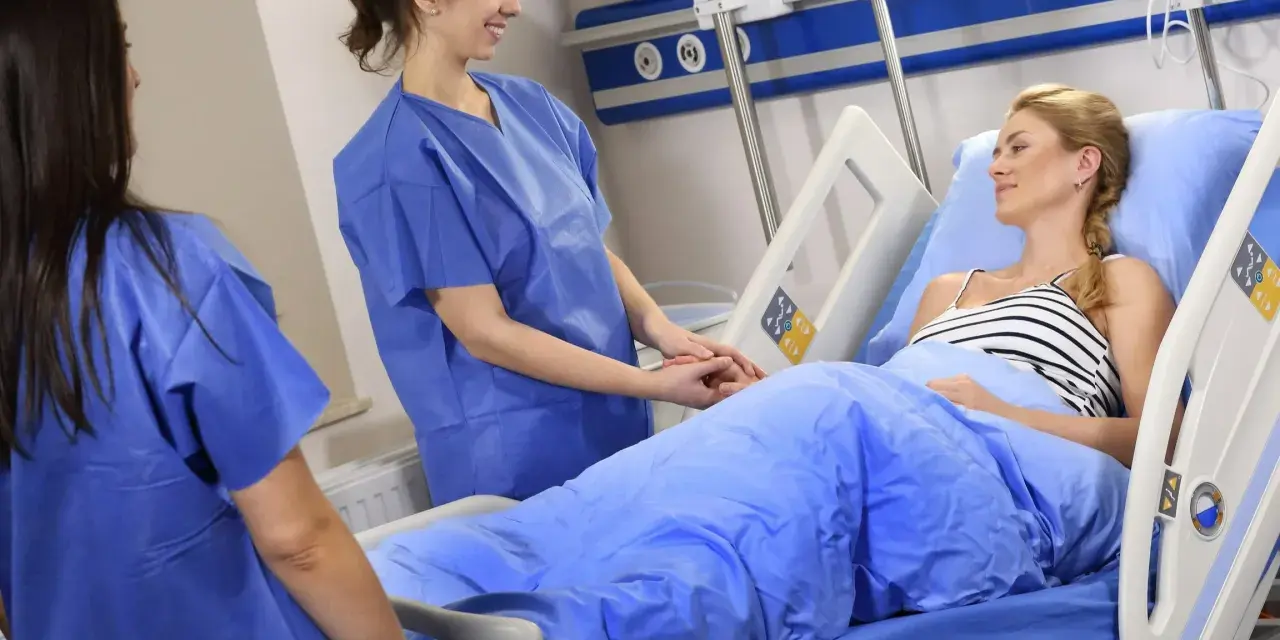 Dwie pielęgniarki w niebieskich fartuchach troskliwie opiekują się pacjentką w łóżku szpitalnym. Czy to CMV?