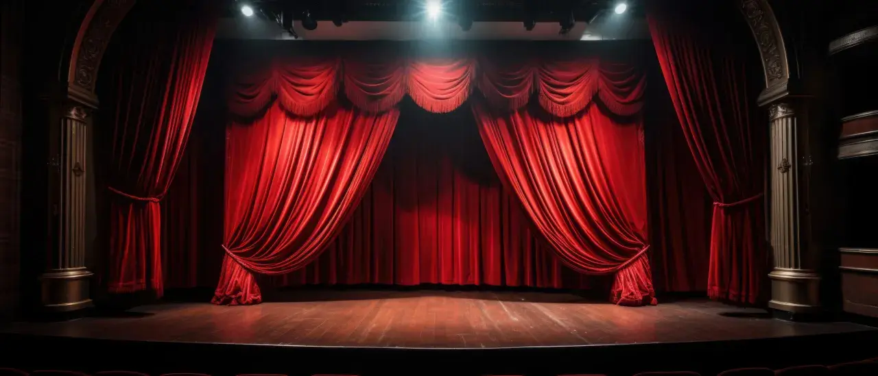 Czerwone, aksamitne zasłony w teatrze, gotowe do odsłonięcia sceny. Podłoga lśni, a światła z góry oświetlają pustą przestrzeń, czekającą na spektakl.