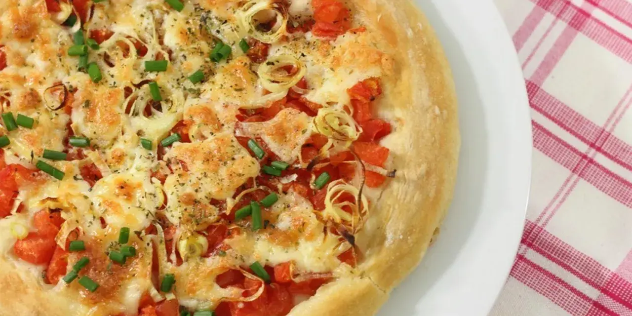 Pizza casera con tomates, queso derretido, cebolla y cebollino. Los ingredientes de esta pizza casera lucen deliciosos.