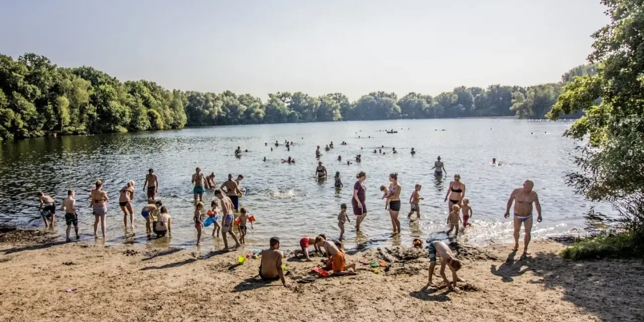 Menschen genießen einen sonnigen Tag im Strandbad Hamburg. Kinder spielen im Sand, während Erwachsene im Wasser planschen.