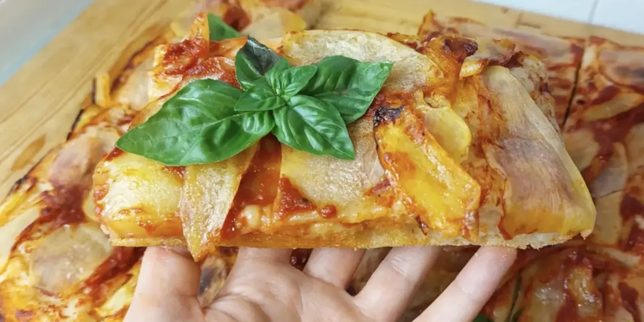 Una fetta di pizza di patate dorata, guarnita con basilico fresco, pronta per essere gustata.
