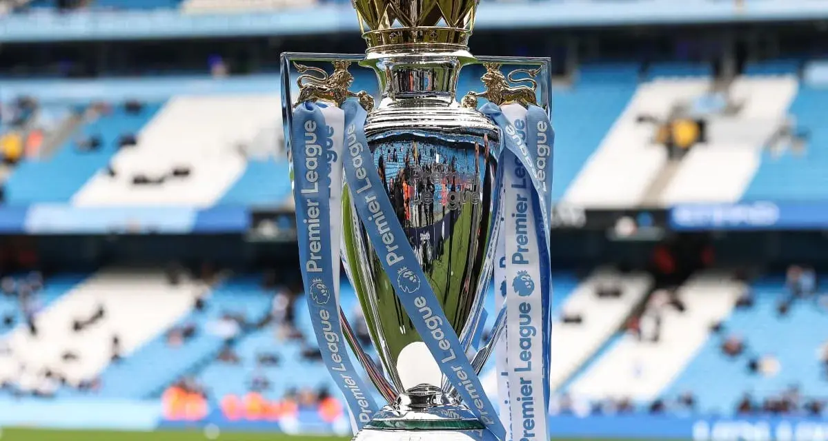 Trofeum za mistrzostwo Anglii, błyszczące i ozdobione wstążkami Premier League, stoi na tle stadionu.