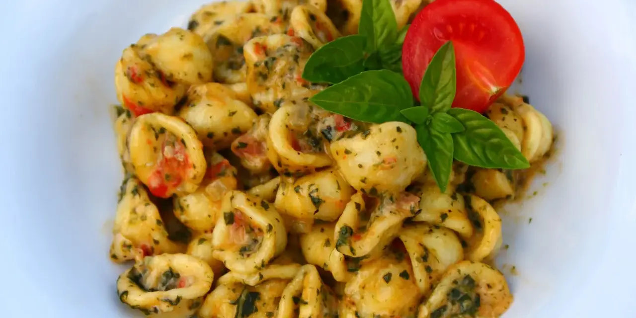 Pyszne makaron orecchiette z sosem pomidorowo-ziołowym, udekorowane listkami bazylii i pomidorem.