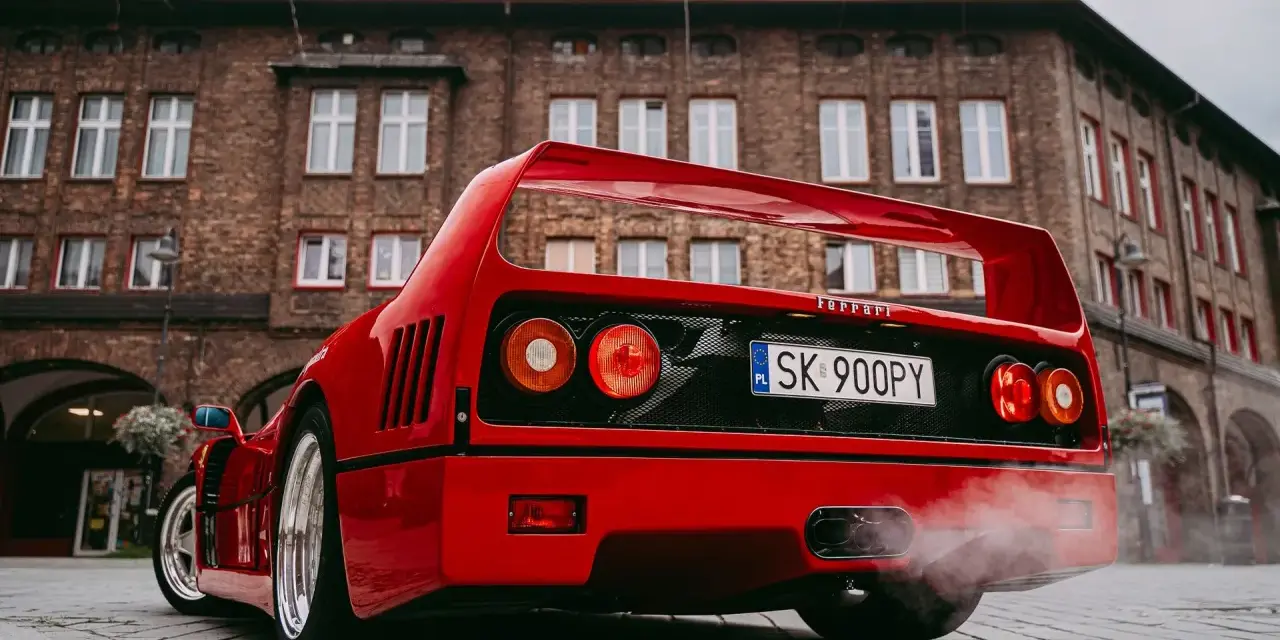 Czerwone Ferrari F40 z dymem z wydechu na tle ceglanego budynku.