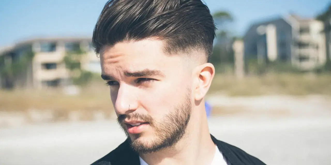 Joven con barba y cortes de pelo hombre elegante, peinado hacia atrás con degradado.