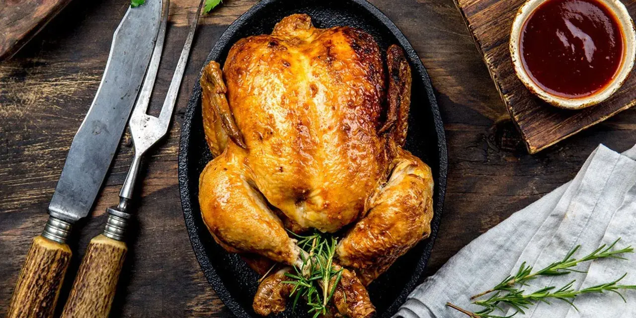 Pollo al horno dorado y jugoso, servido en sartén de hierro fundido con romero. Acompañado de salsa barbacoa y cubiertos rústicos.