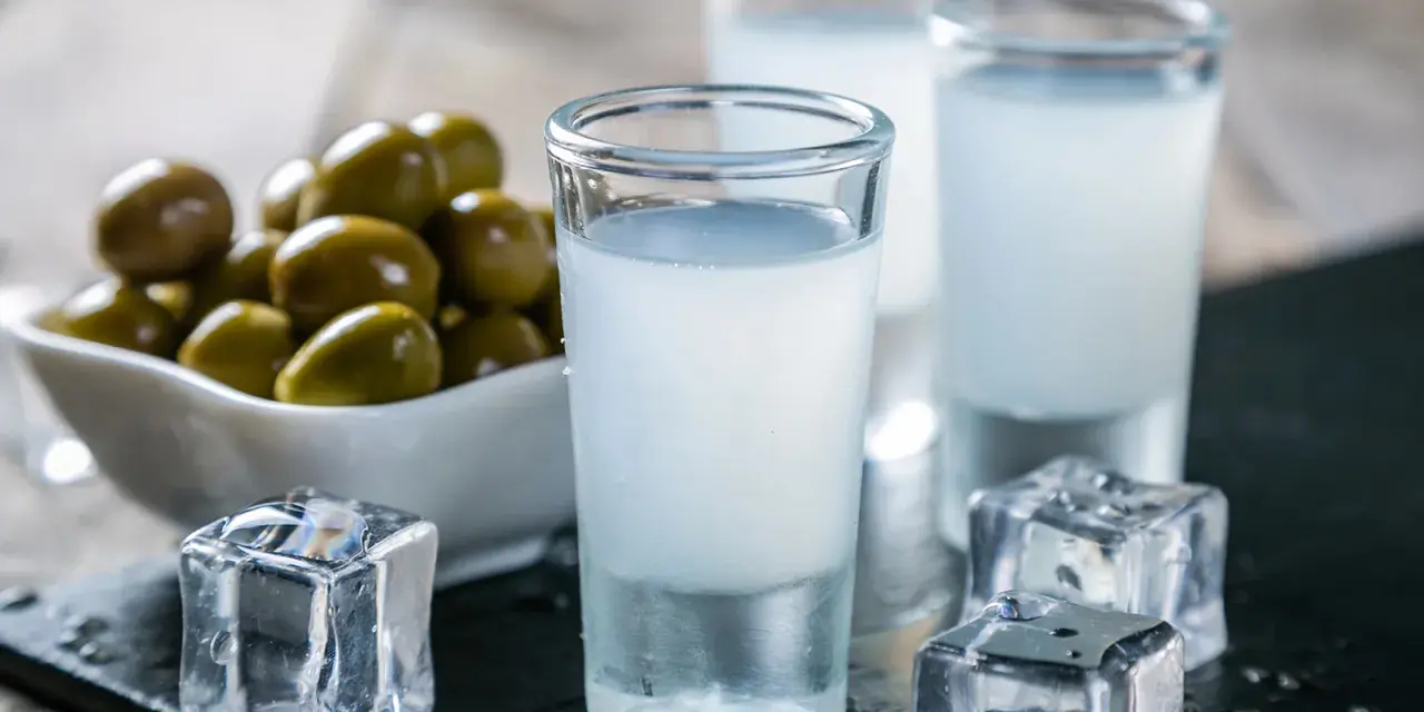 Raki, ein Getränk, das oft mit Griechenland assoziiert wird, wird aus Trauben hergestellt. Hier sind Gläser mit Raki, Eiswürfel und Oliven.