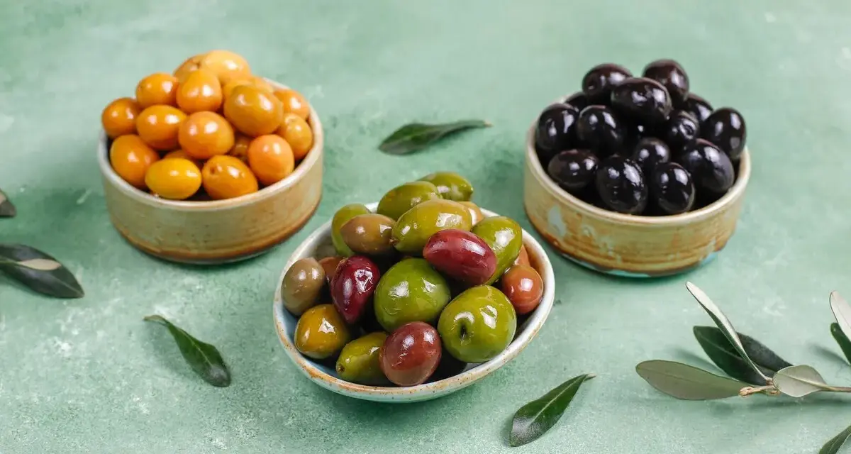 Tres cuencos con aceitunas de diferentes colores: amarillas, verdes y negras.