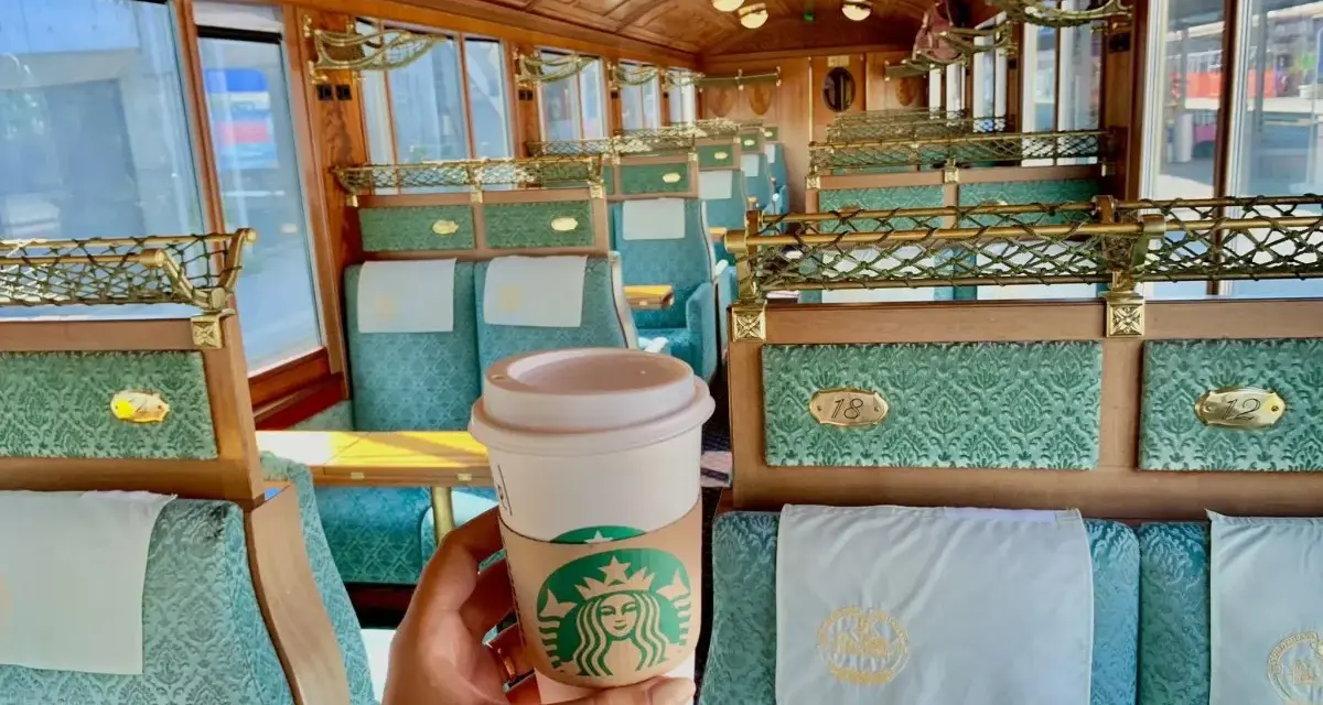 Enjoying a Starbucks coffee in the opulent, Belle Époque-style interior of a train, a stark contrast to modern panoramic views.