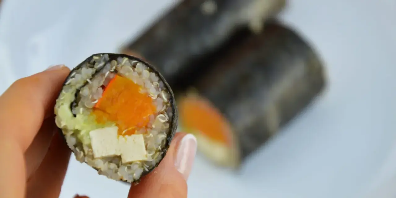 Rolka sushi z tofu, dynią i awokado, trzymana w dłoni.