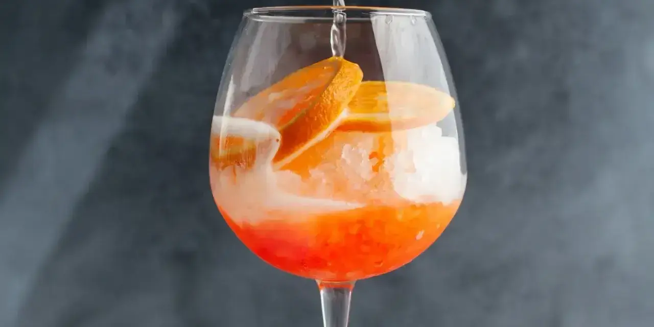 Orzeźwiający drink z cydrem, lodem i plasterkami pomarańczy, przygotowywany w dużym kieliszku.
