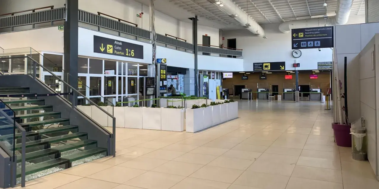 Inside an airport terminal, signs point to boarding gates 1-6. This is likely the closest airport to San Sebastian.