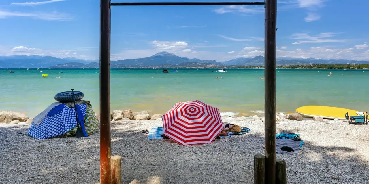 Słoneczne plaże nad Jeziorem Garda, z turkusową wodą, górami w tle i kolorowymi parasolami.