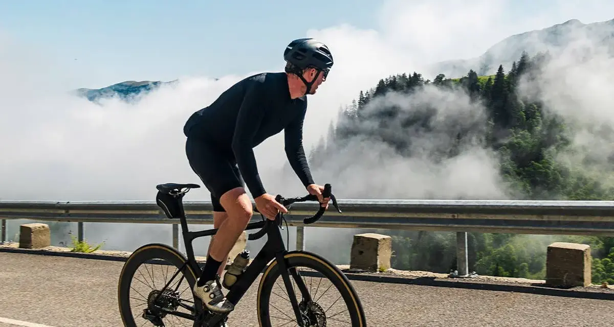 A cyclist in black gear conquers a mountain road, enjoying the breathtaking views and the freedom of long rides amidst swirling clouds.