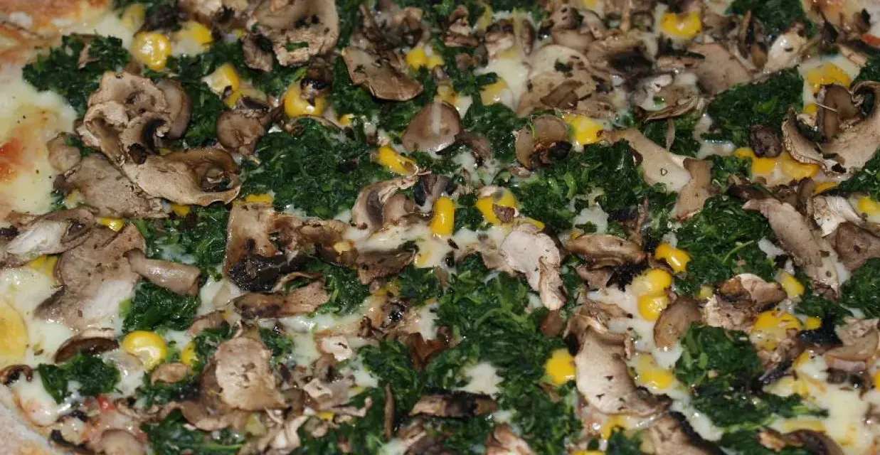 Pyszna pizza ze szpinakiem, grzybami i kukurydzą, obficie posypana serem.