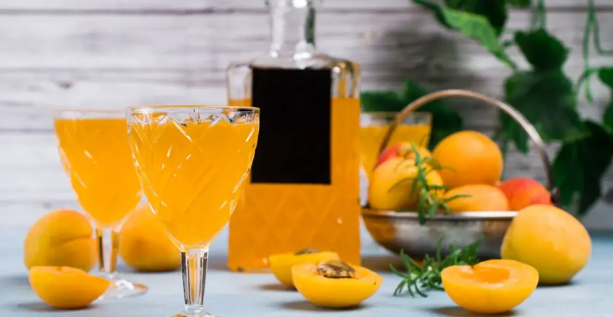 Orzeźwiający drink z likierem brzoskwiniowym, podany w eleganckich kieliszkach, z owocami i butelką w tle.