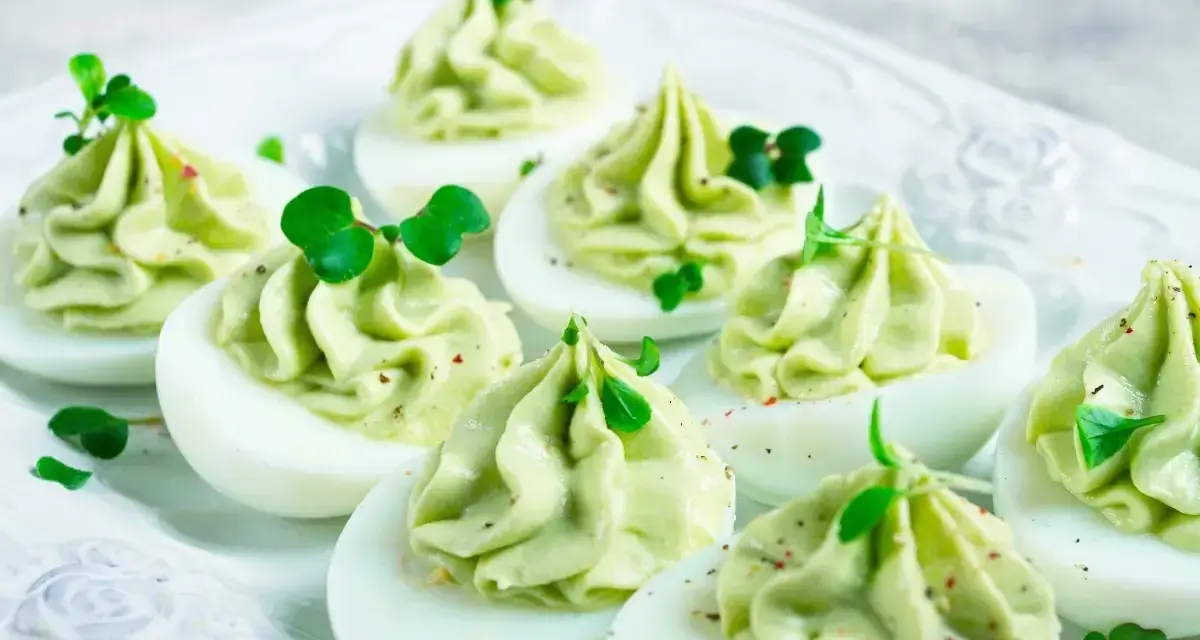 Uova ripiene pasquali, guarnite con crema verde e germogli freschi, pronte per essere gustate.