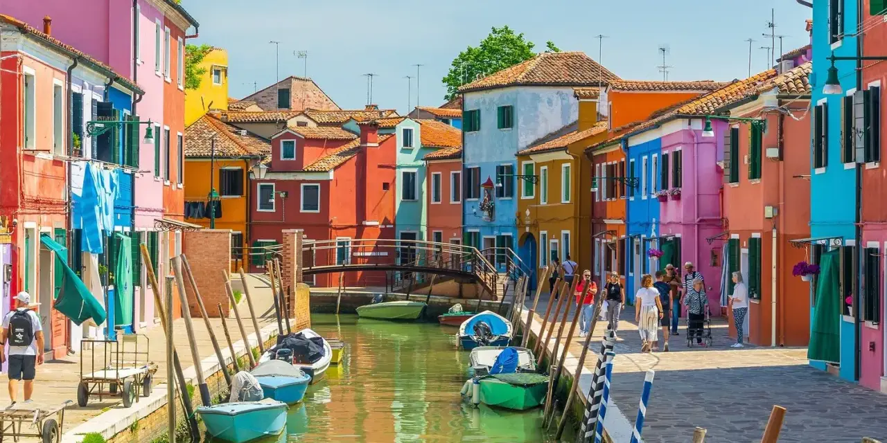 Colorate case affacciate su un canale a Venezia, con barche ormeggiate e persone che passeggiano. Le fondamenta sono un tripudio di colori vivaci.