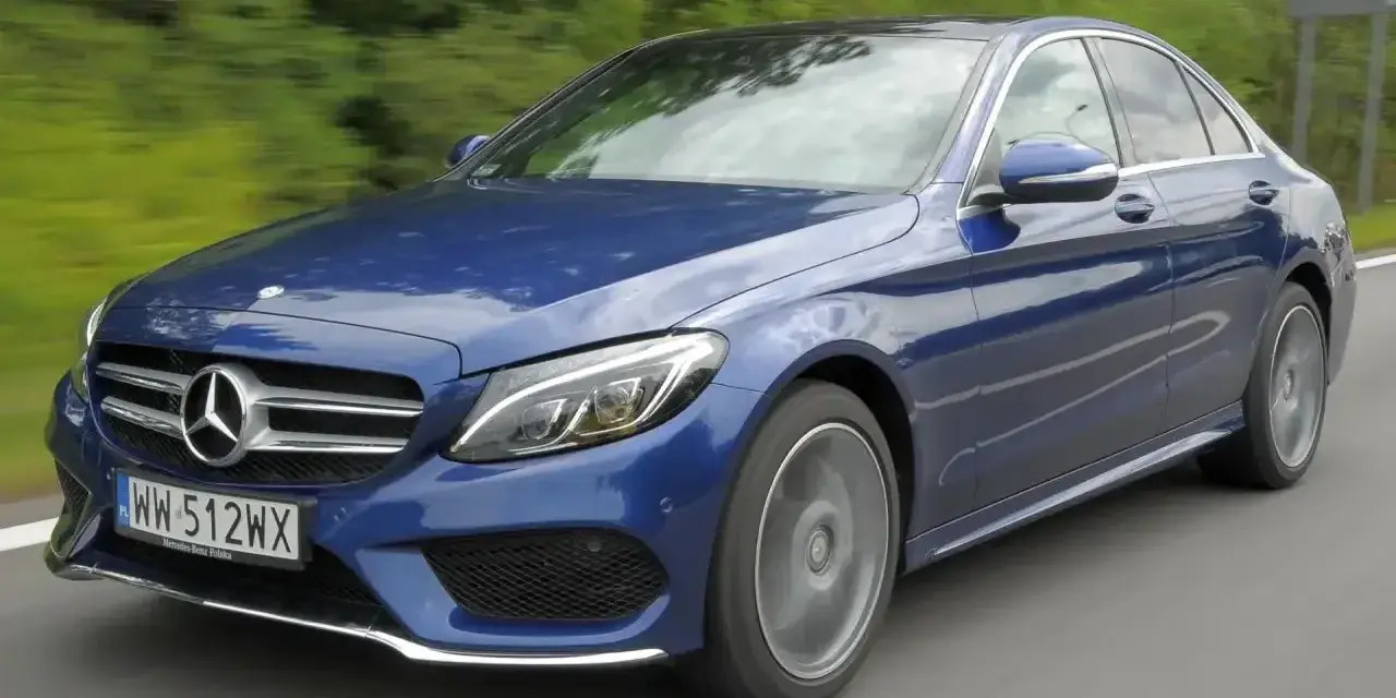 Błękitny Mercedes E220d w ruchu, z rozmytym tłem zieleni i drogi. Elegancki sedan na polskich tablicach rejestracyjnych.