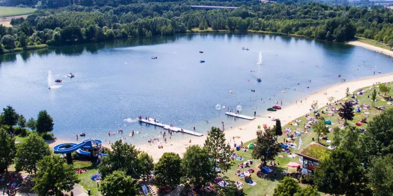 Sommerliche Idylle am Borkener See mit vielen Badegästen, Wasserrutsche und schattigen Plätzen unter Bäumen.