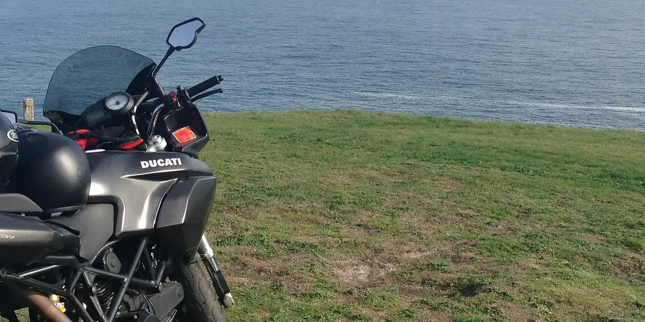 Motocykl Ducati zaparkowany na trawie z widokiem na morze. Marzenie o podróży przez Szwecję motocyklem.